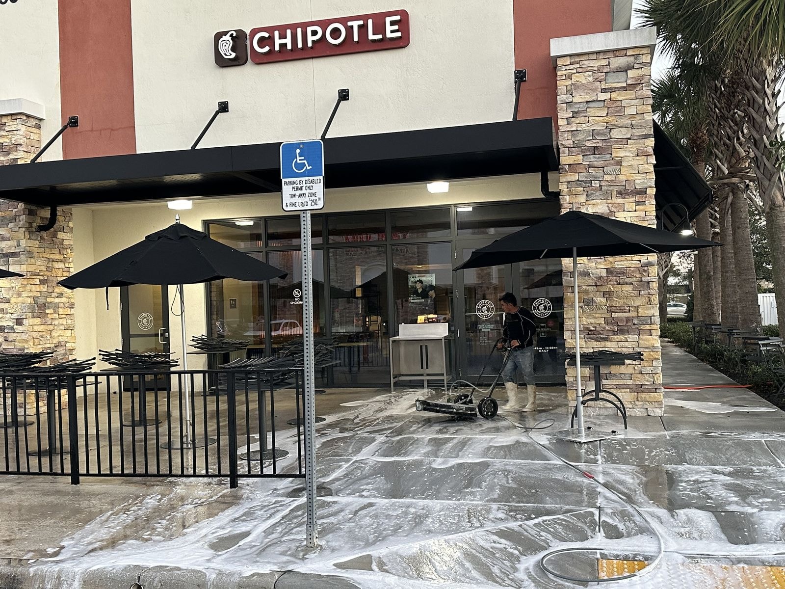 Technician pressure washing a commercial restaurant patio with surface cleaner in Boynton Beach, Florida