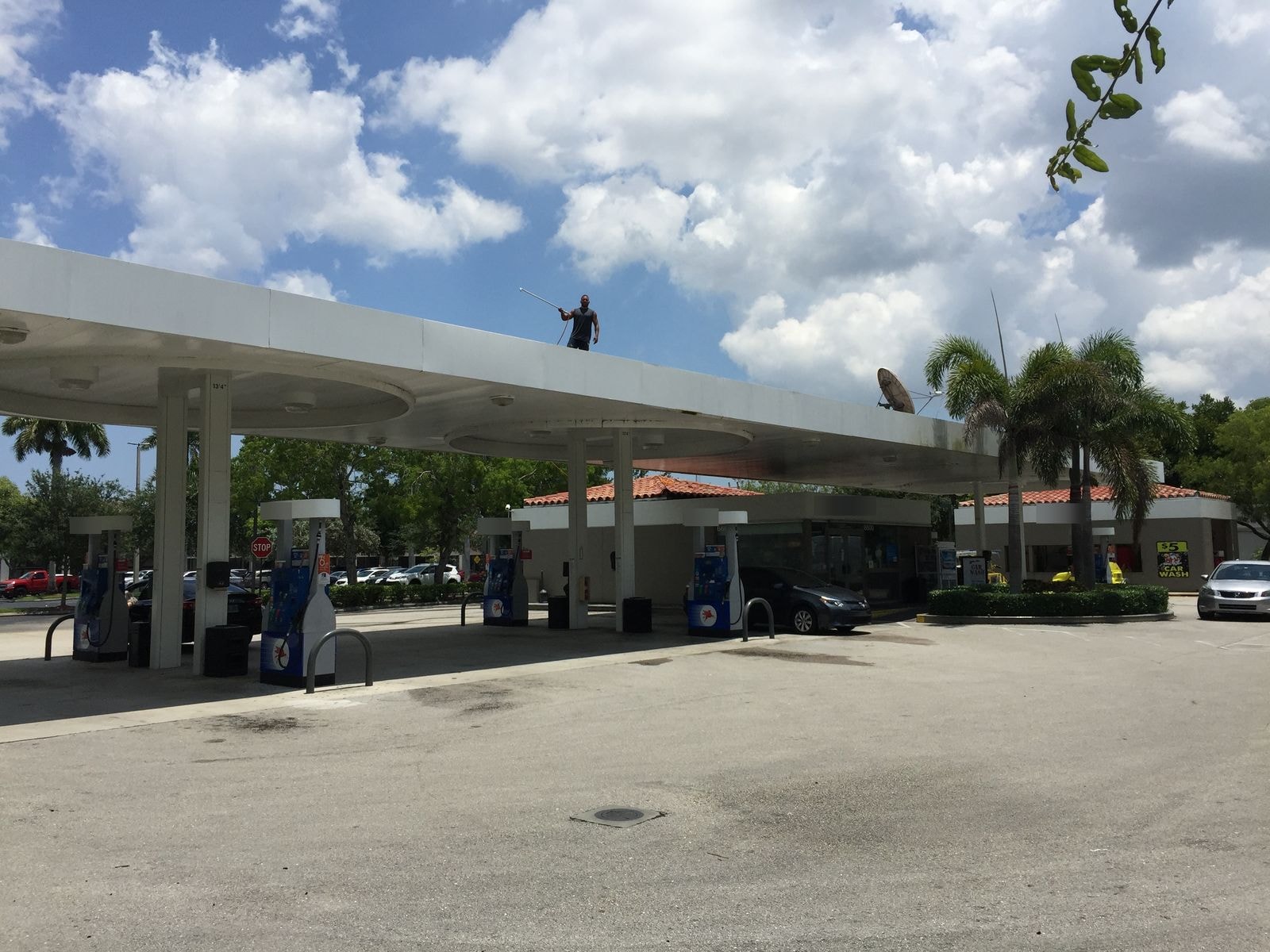 Technician soft-washing a gas station fuel island canopy in Coconut Creek, Florida