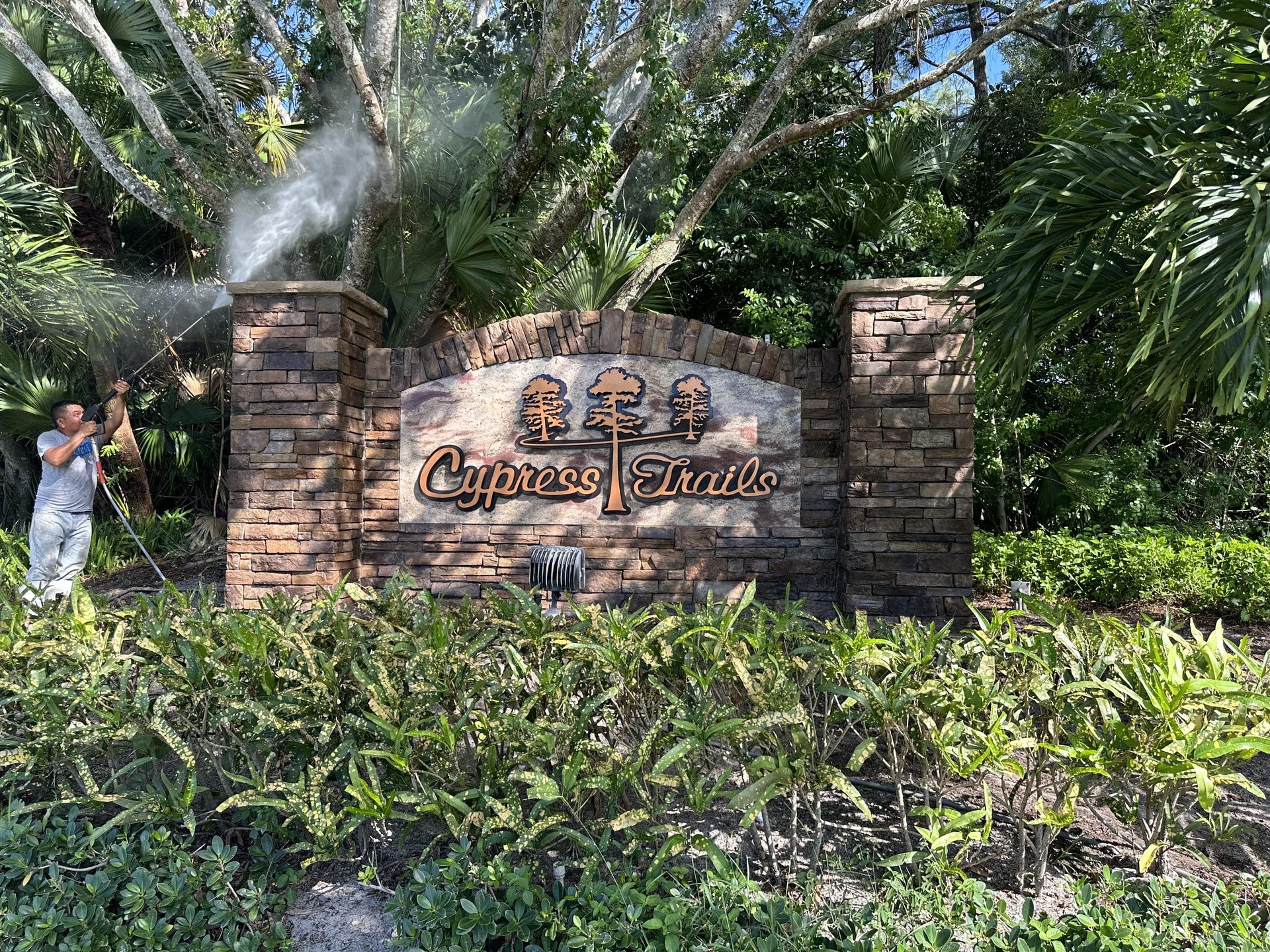 Technician soft-washing a stacked stone HOA entrance monument sign, Lake Worth, FL