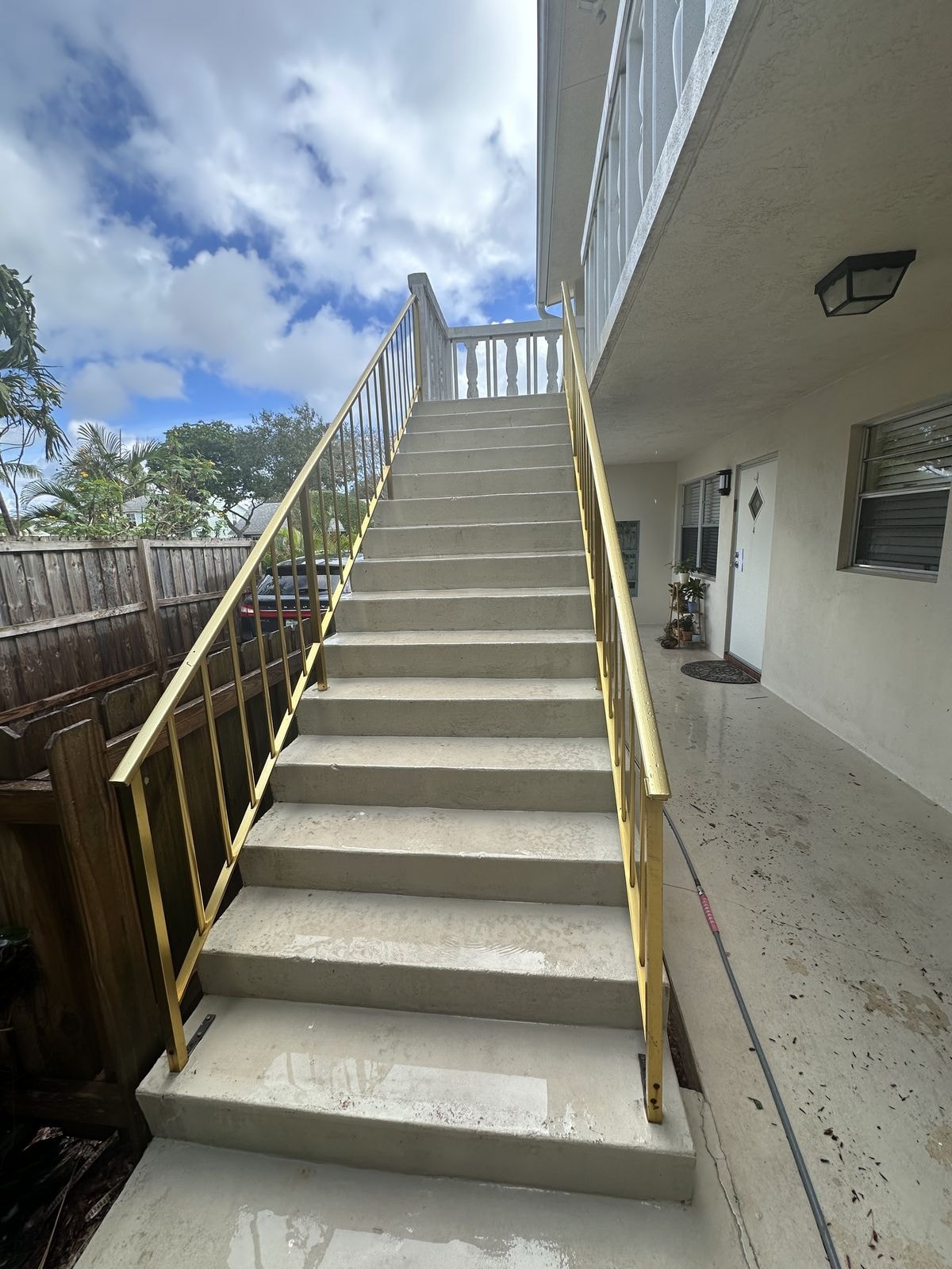 After: Before and after pressure washing of concrete stairs with gold metal railings — heavy algae staining fully removed, Lake Worth, FL