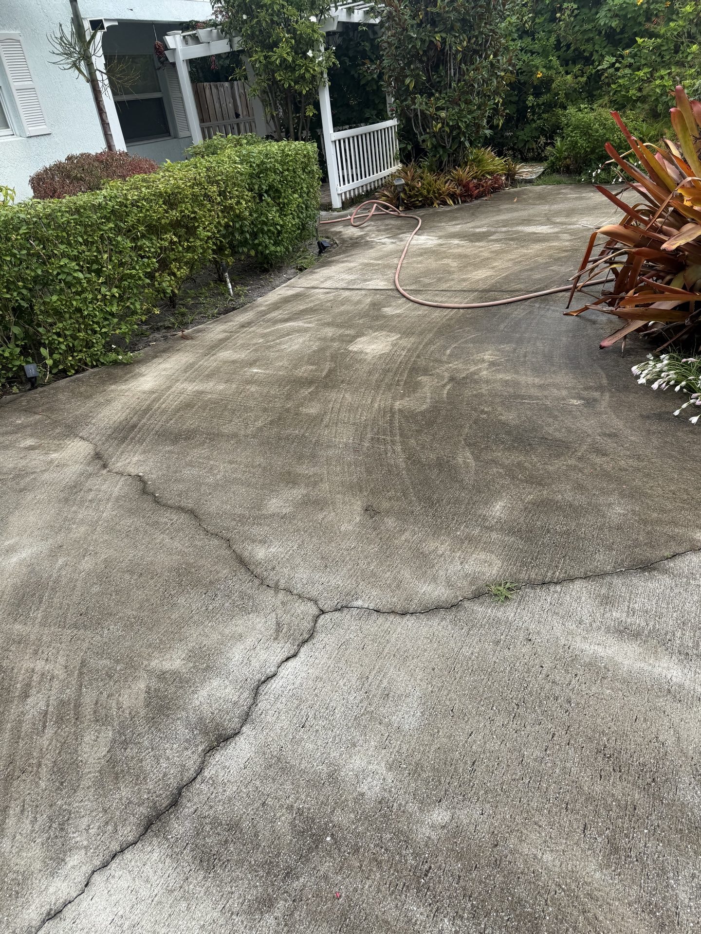 Before: Concrete driveway with algae staining, tire-track discoloration, and settlement cracking before pressure washing, Boynton Beach, FL