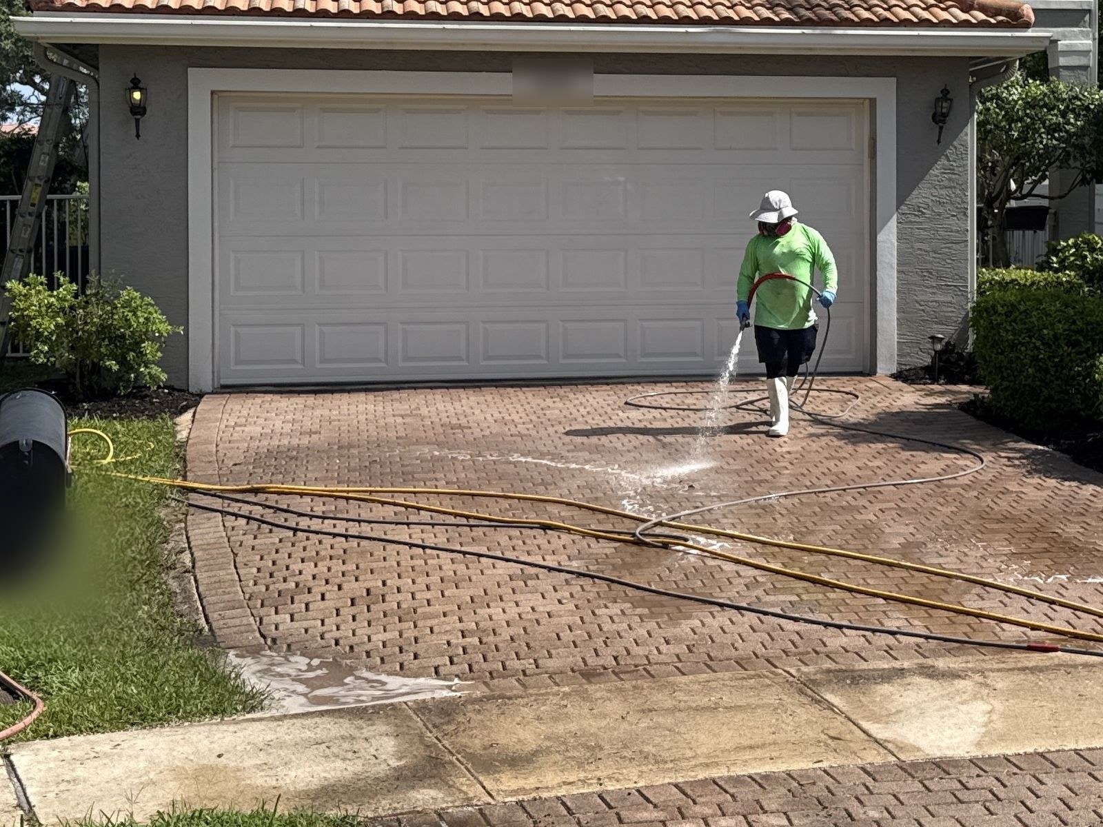 Before: Technician pressure washing a brick paver driveway, staining still visible on the untreated section, Greenacres, FL