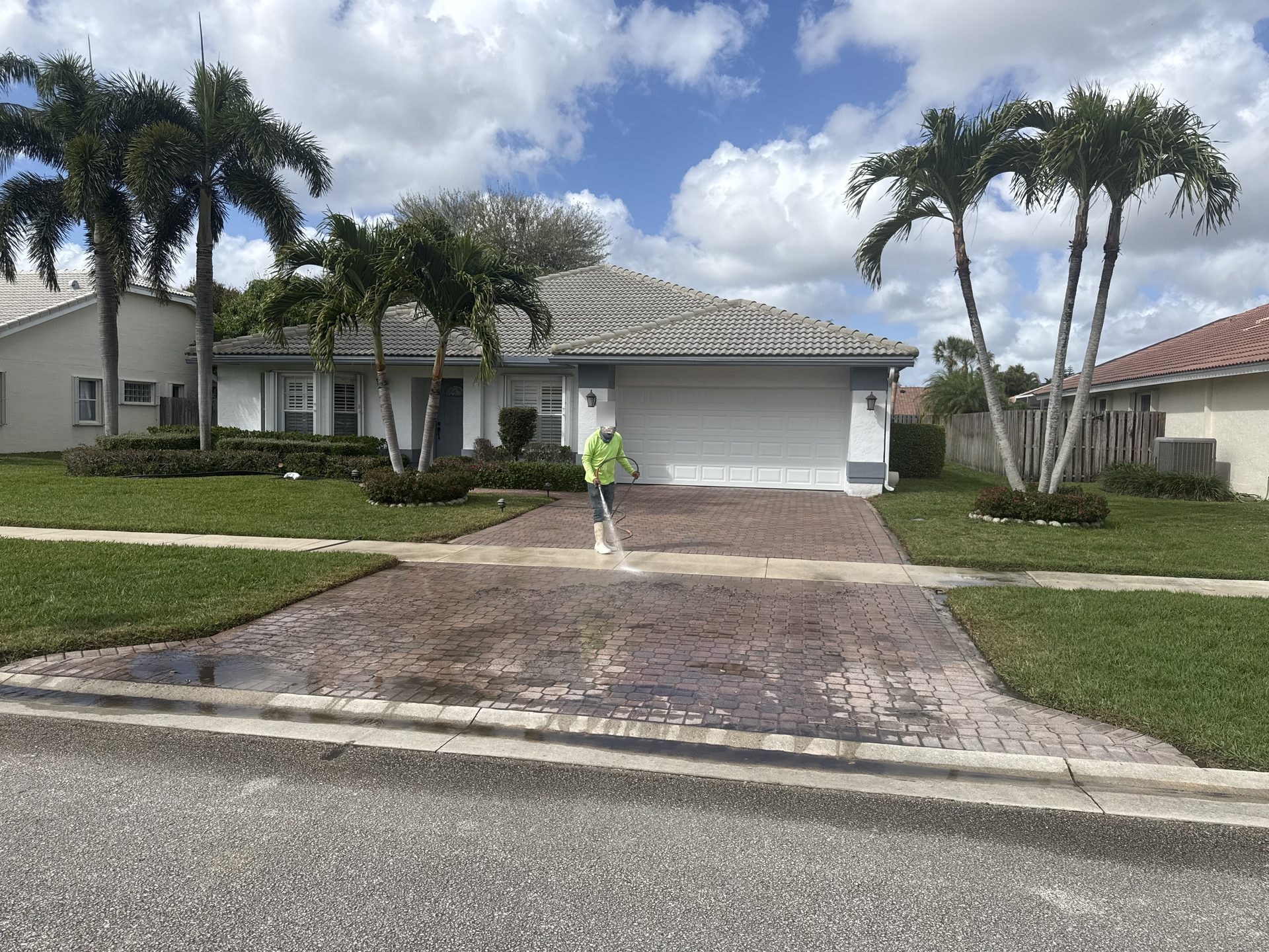 Before: Brick paver driveway during pressure washing with staining still visible, technician spraying the surface, Lake Worth, FL