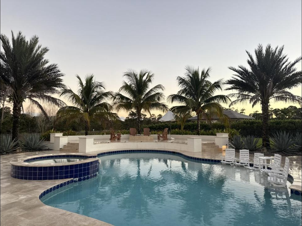 Travertine pool deck and pool at a Jupiter, FL estate at dusk — palm trees, spa and fire pit area in background