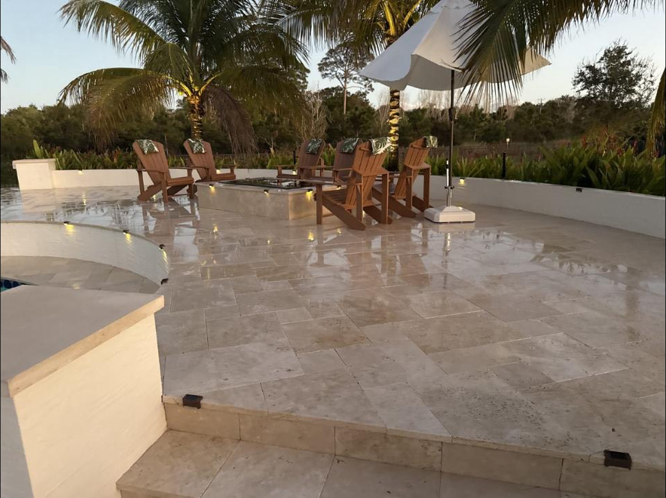 Travertine pool deck with fire pit seating area at a Jupiter, FL estate — deck still wet after pressure washing, dusk