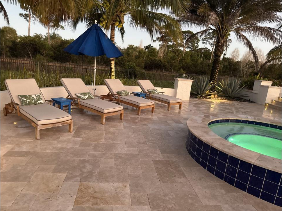 Travertine pool deck with loungers and spa surround at a Jupiter, FL estate — freshly pressure washed, dusk
