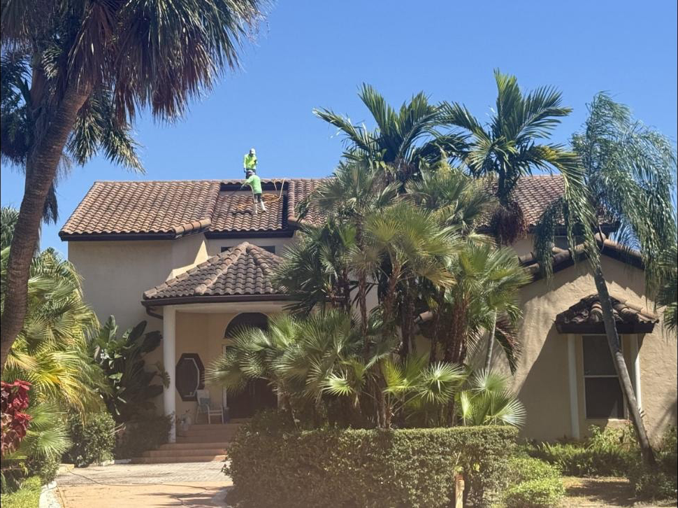 After: Front entrance of Lake Worth Beach, FL waterfront home — technician on roof during soft-wash cleaning in progress