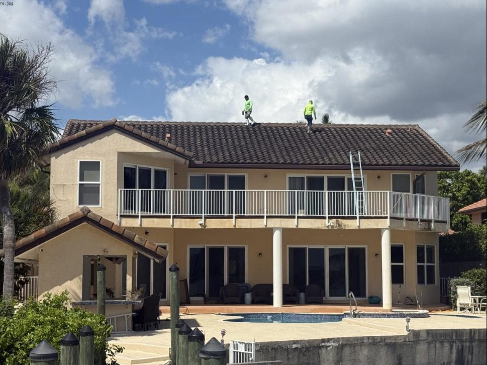 Before: Waterfront home barrel tile roof in Lake Worth Beach, FL before soft-wash cleaning — two technicians on roof