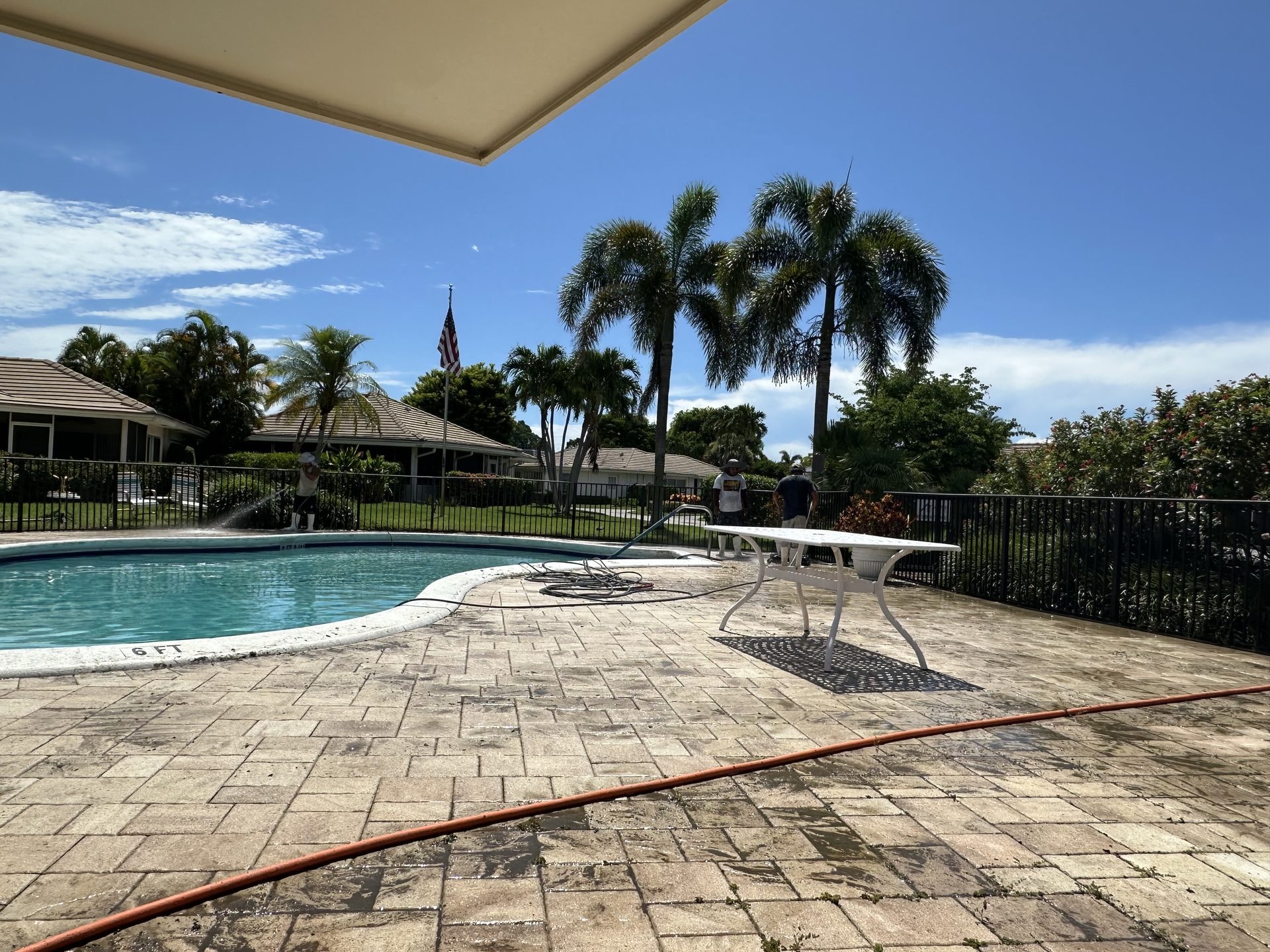 Before: Community pool deck with staining on the paver surface before cleaning, technicians working on site, Atlantis, FL