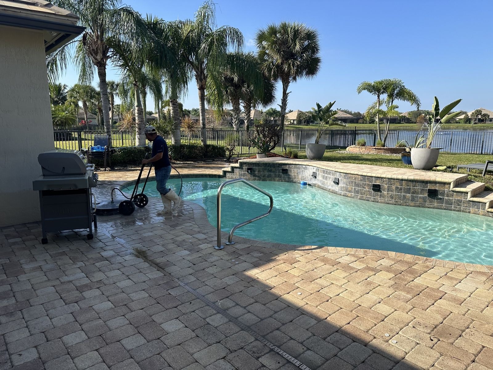 Before: Paver pool deck being pressure washed, technician working with surface cleaner, Wellington, FL