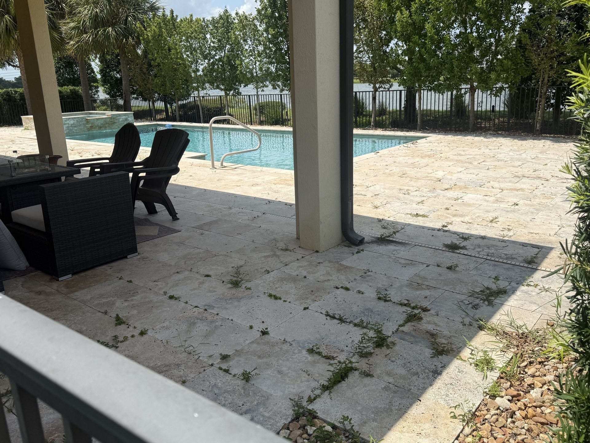 Before: Travertine pool deck with weed growth and organic staining in the joints before cleaning, lakefront home, Wellington, FL