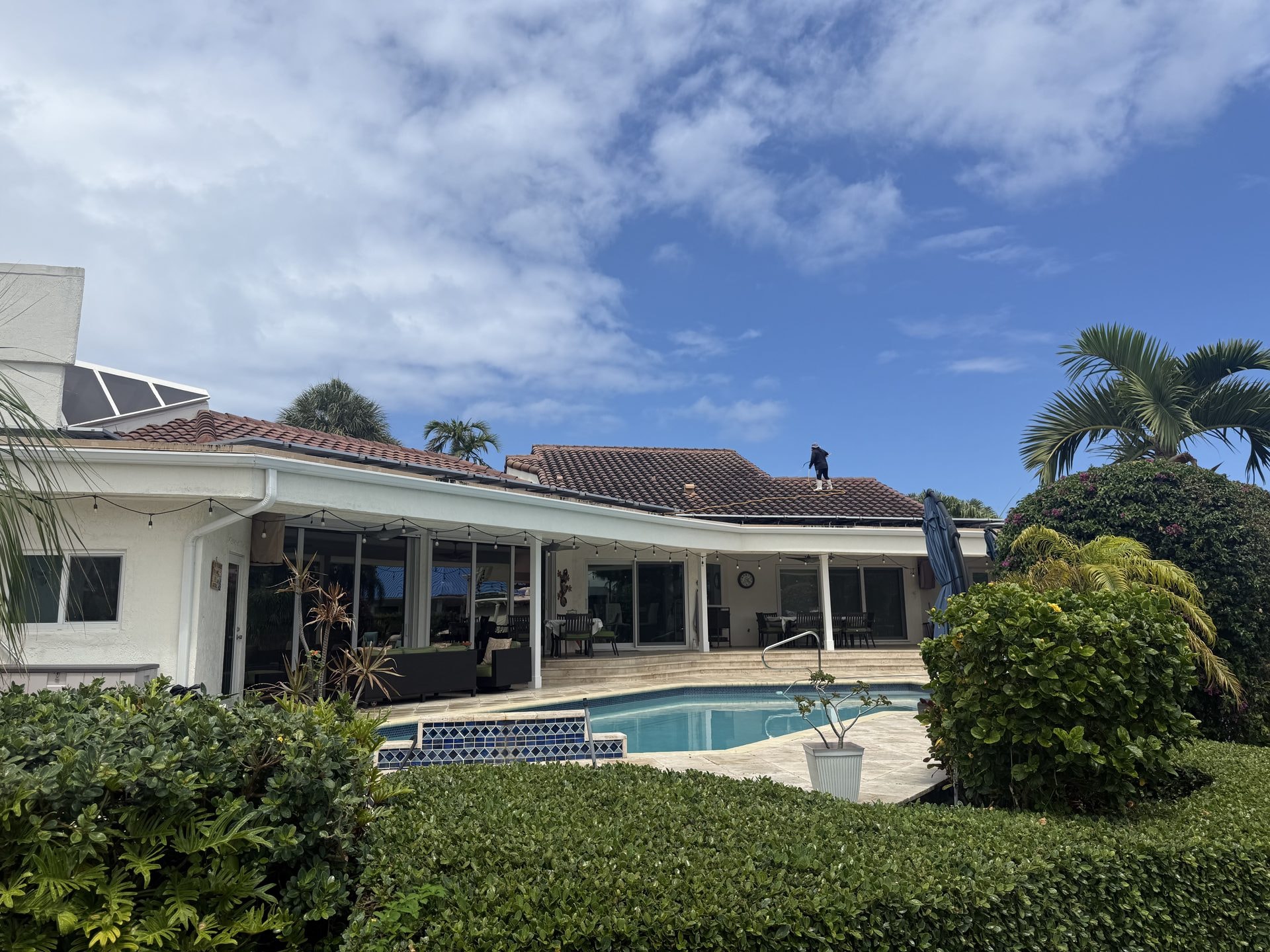 Before: Barrel tile roof with heavy algae staining before soft-wash cleaning, technician working on the roof of a waterfront pool home, Boca Raton, FL