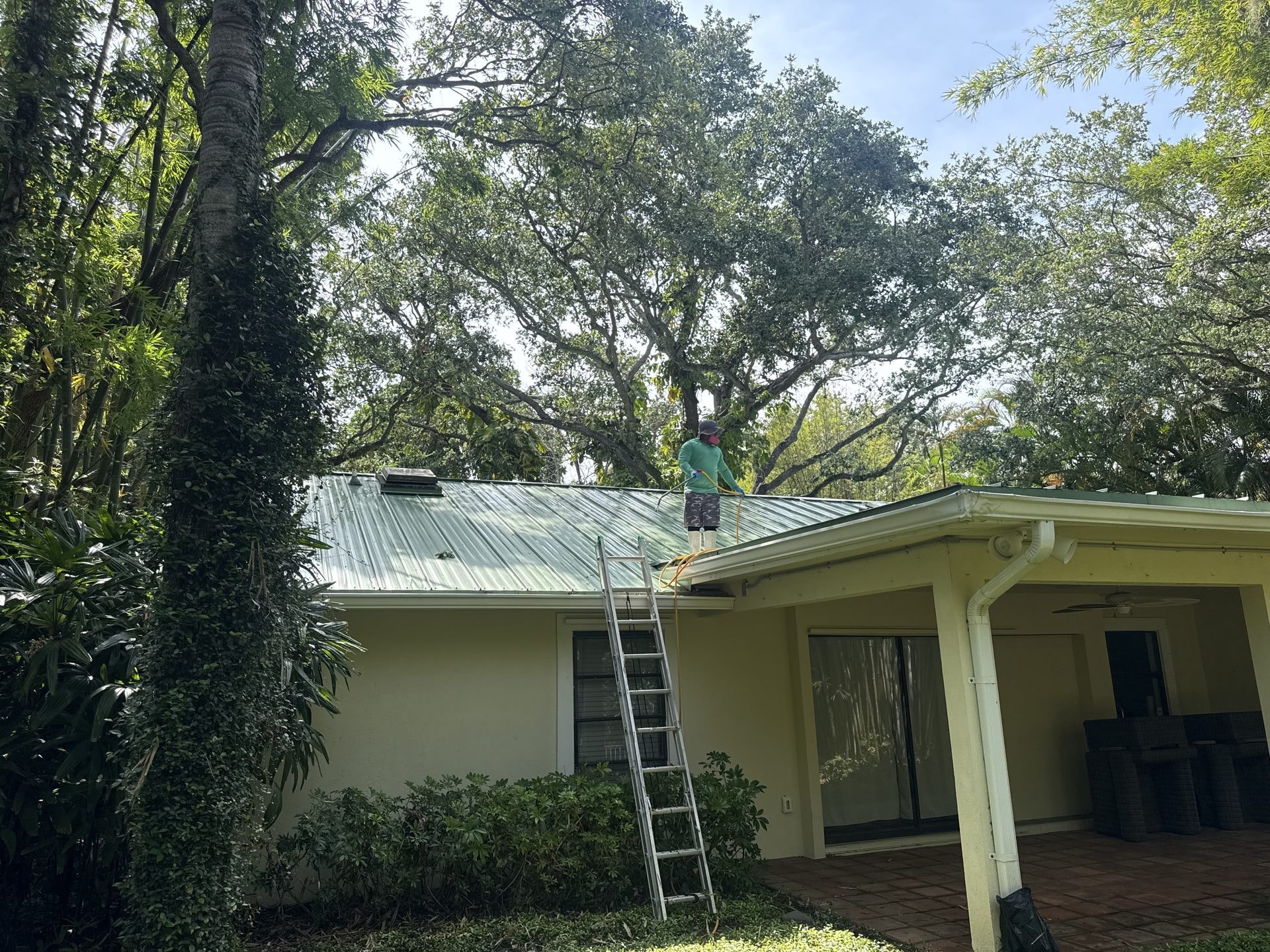 Before: Standing seam metal roof with weathered discoloration before cleaning, technician applying low-pressure soft-wash solution, Palm Beach Gardens, FL