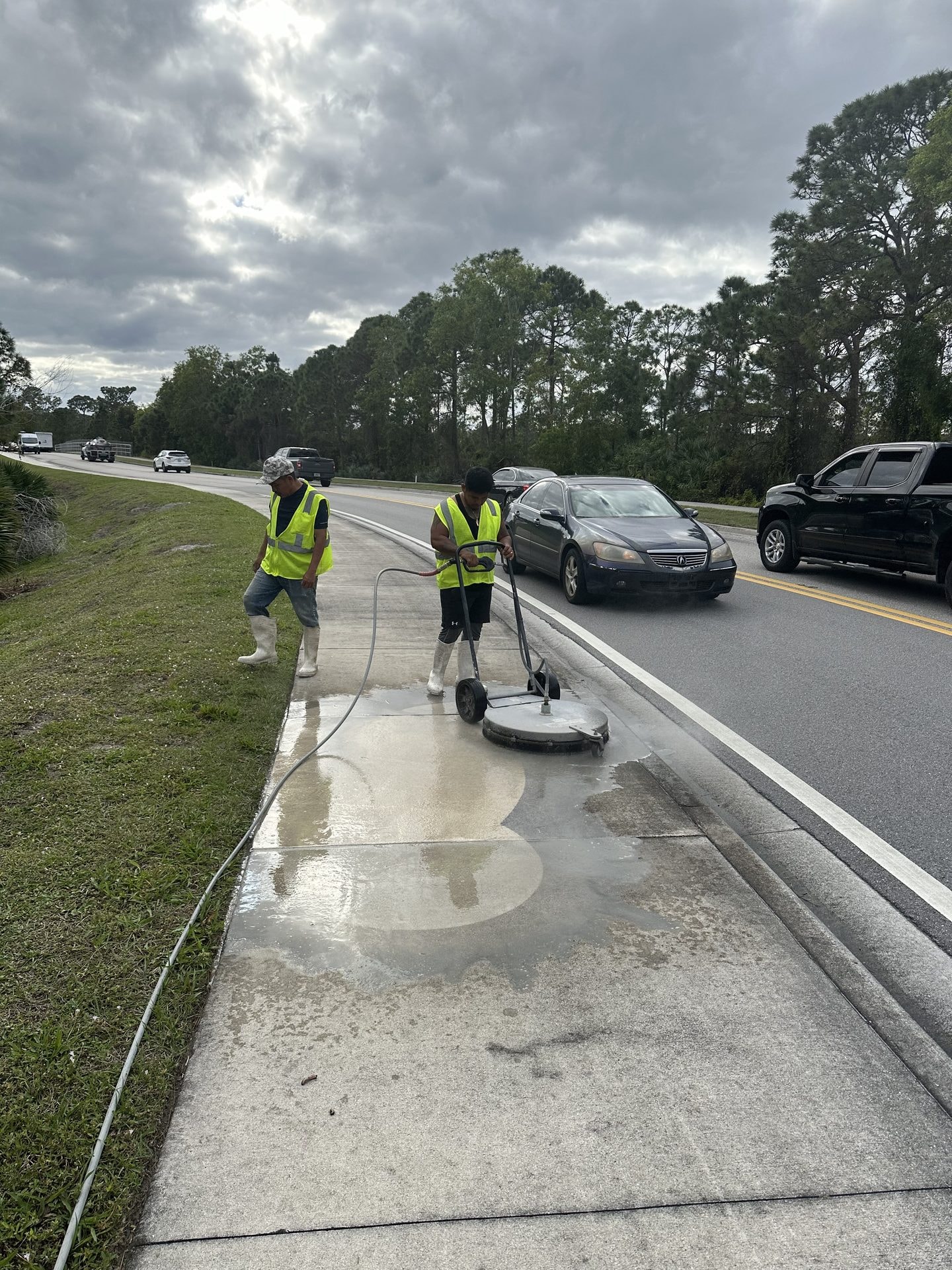 Crew in high visibility vests cleaning HOA-maintained public sidewalk with a surface cleaner alongside a roadway, Jupiter, FL