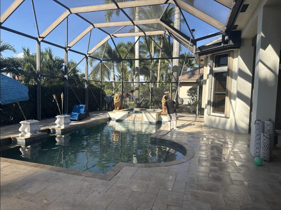 Technician rinsing pool screen enclosure at a Wellington, FL estate — travertine deck and lion statues