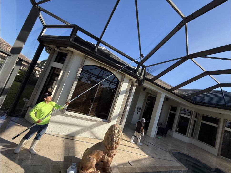Two-man crew cleaning pool screen enclosure at a Wellington, FL estate — one technician on extension pole
