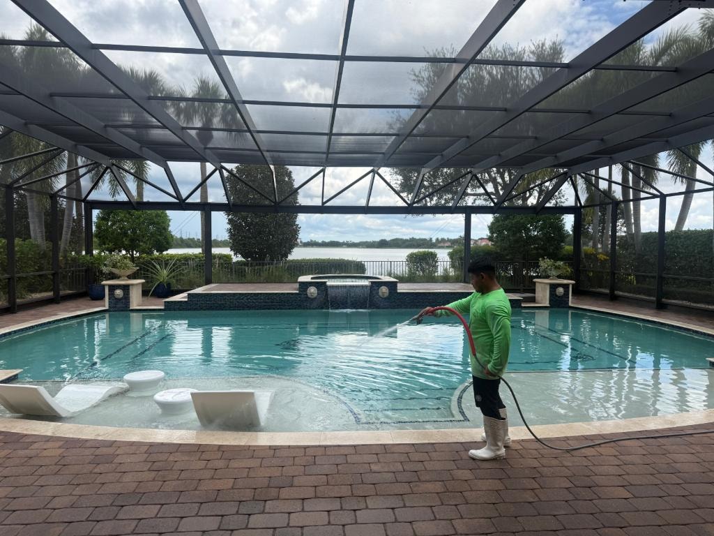 Crew pressure washing a brick paver pool deck inside a lakefront pool screen enclosure in Wellington, FL