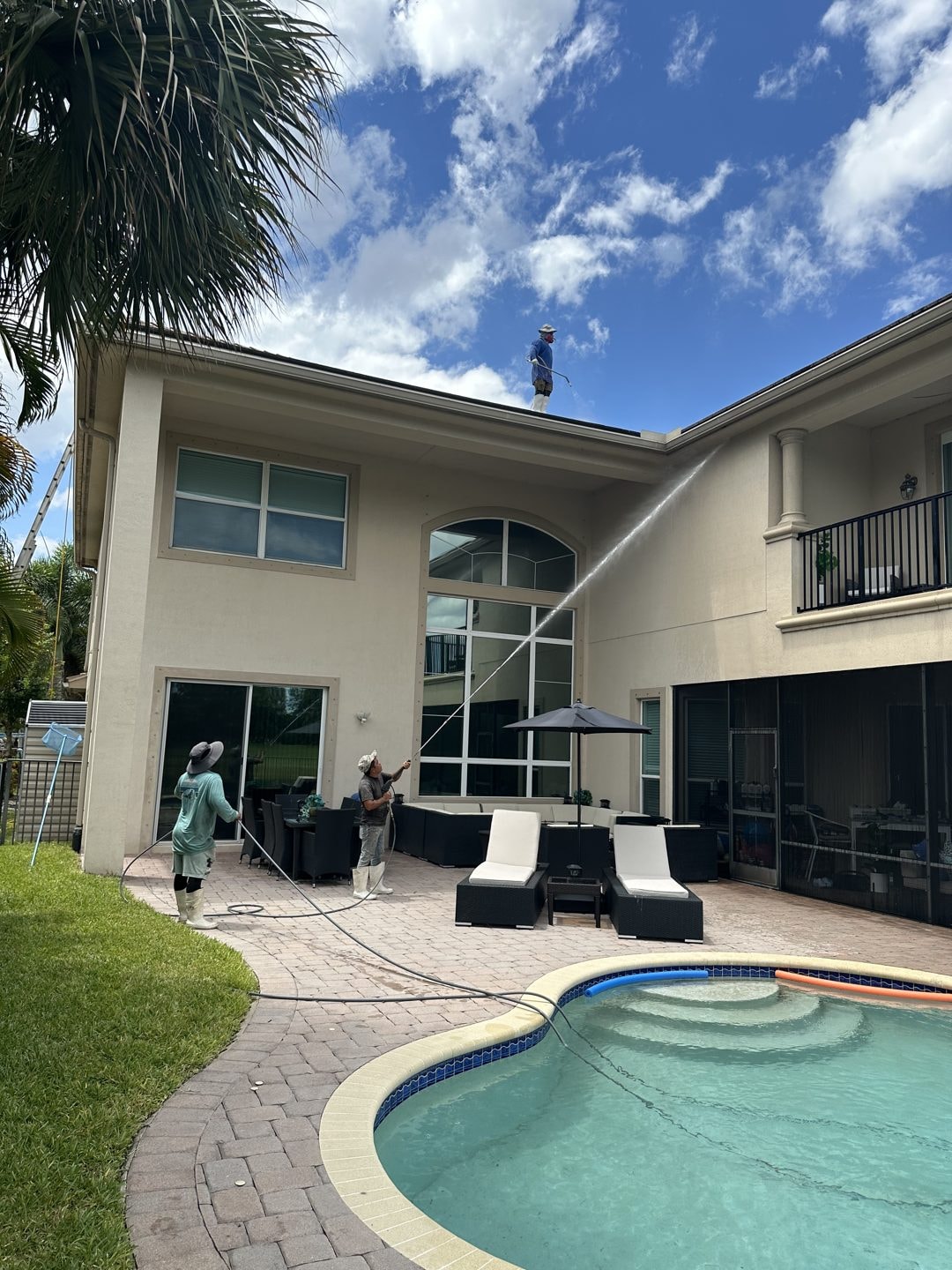 Technician soft-washing a two-story tile roof while two crew members wash the house walls in Wellington, FL