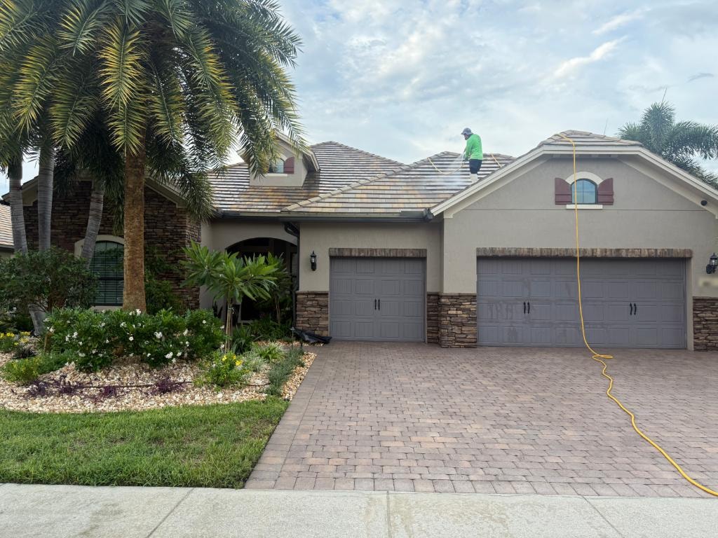 Technician soft washing a multicolor flat tile roof at a Wellington, FL home, with a visible clean line across the slope
