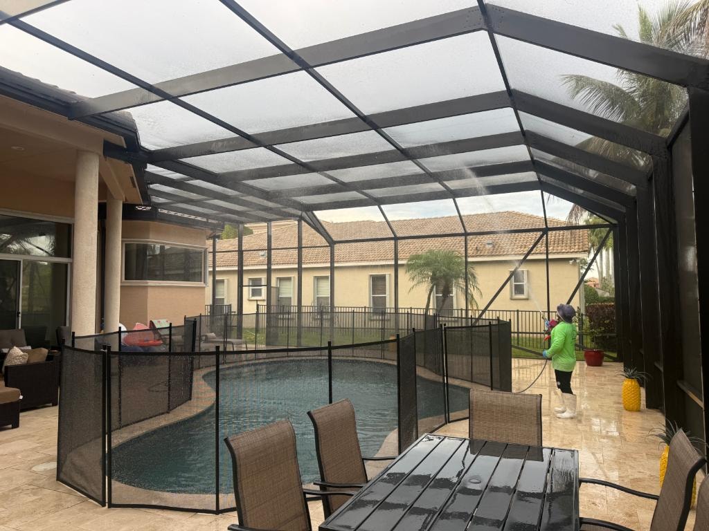 Crew pressure washing a travertine pool deck and rinsing the screen enclosure (lanai) at a Wellington, FL home