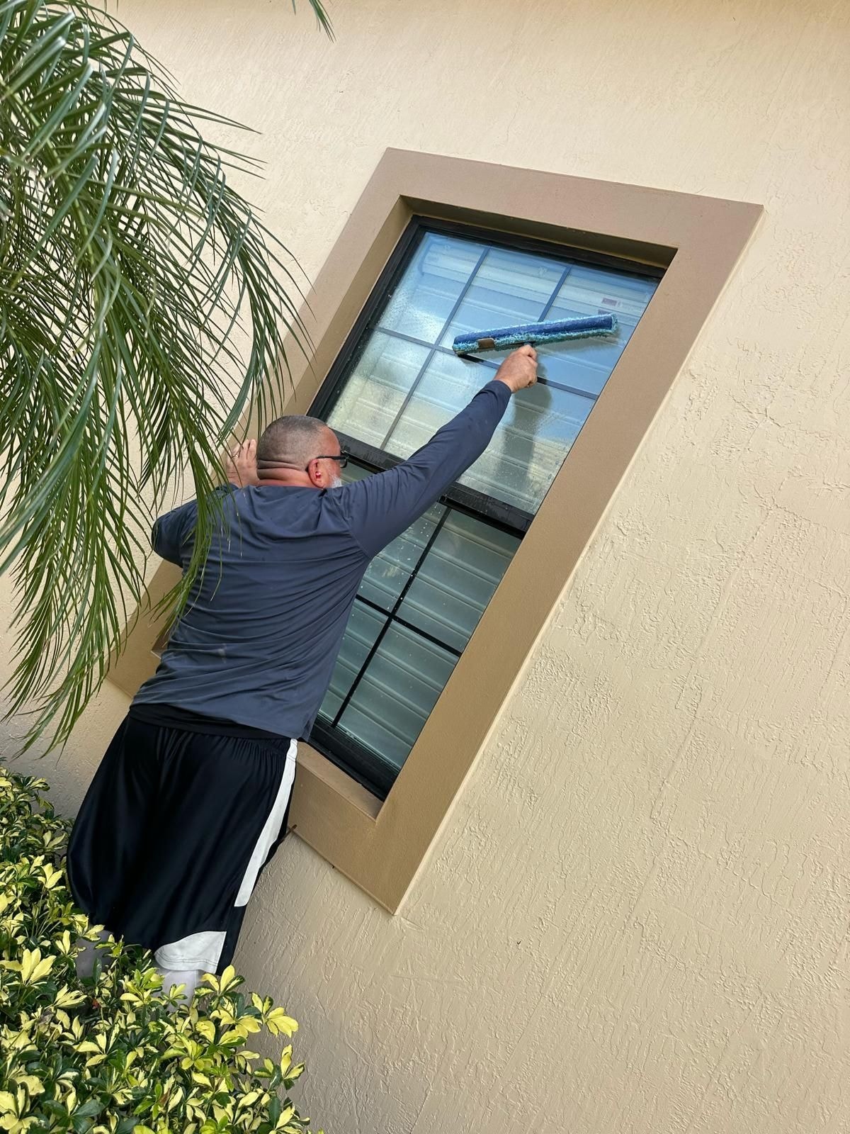 Technician scrubbing exterior window panes on a residential home, Wellington, FL
