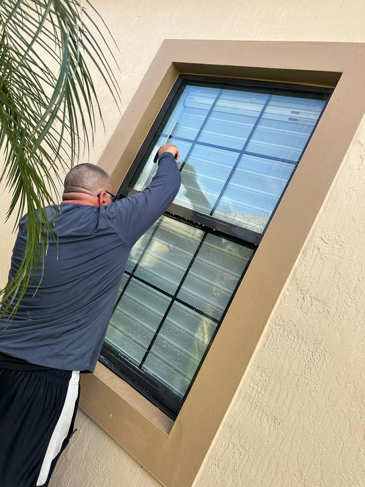Technician using a squeegee to finish cleaning exterior windows on a residential home, Wellington, FL