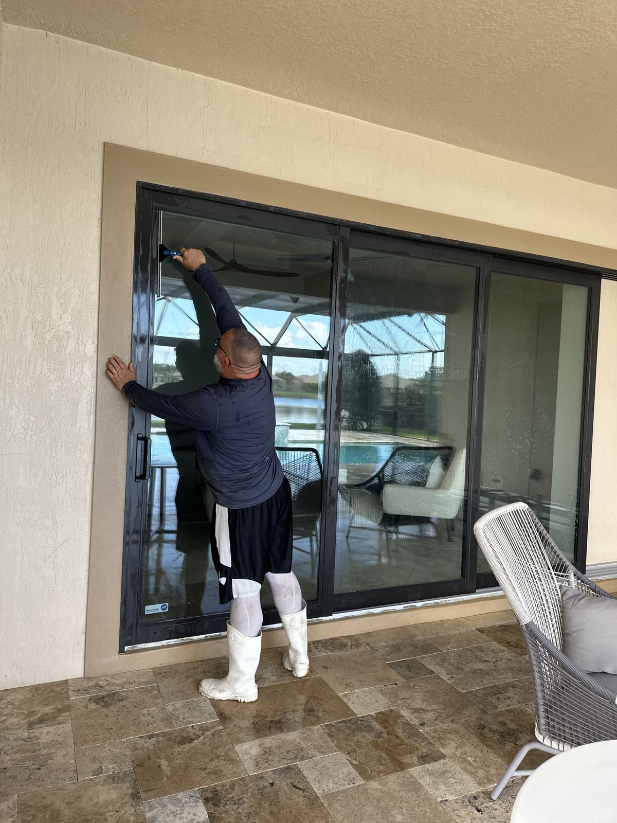 Technician cleaning large sliding glass doors on a luxury pool home with travertine deck and lake view, Wellington, FL