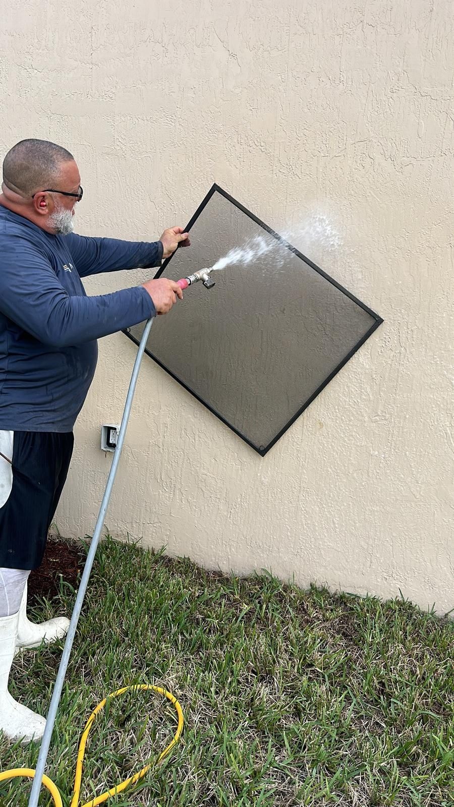 Technician rinsing a removed window screen during professional window cleaning service, Wellington, FL