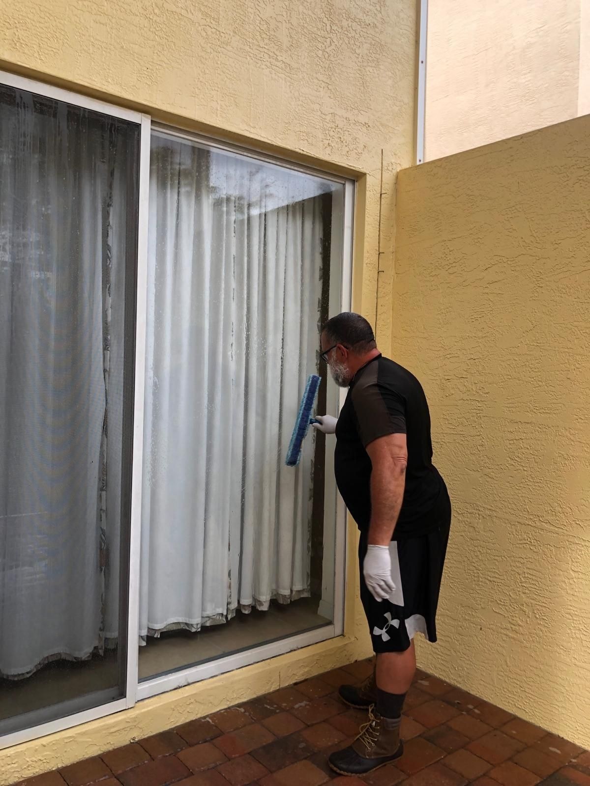 Technician cleaning a large sliding glass door on a commercial or multi-family property, Wellington, FL