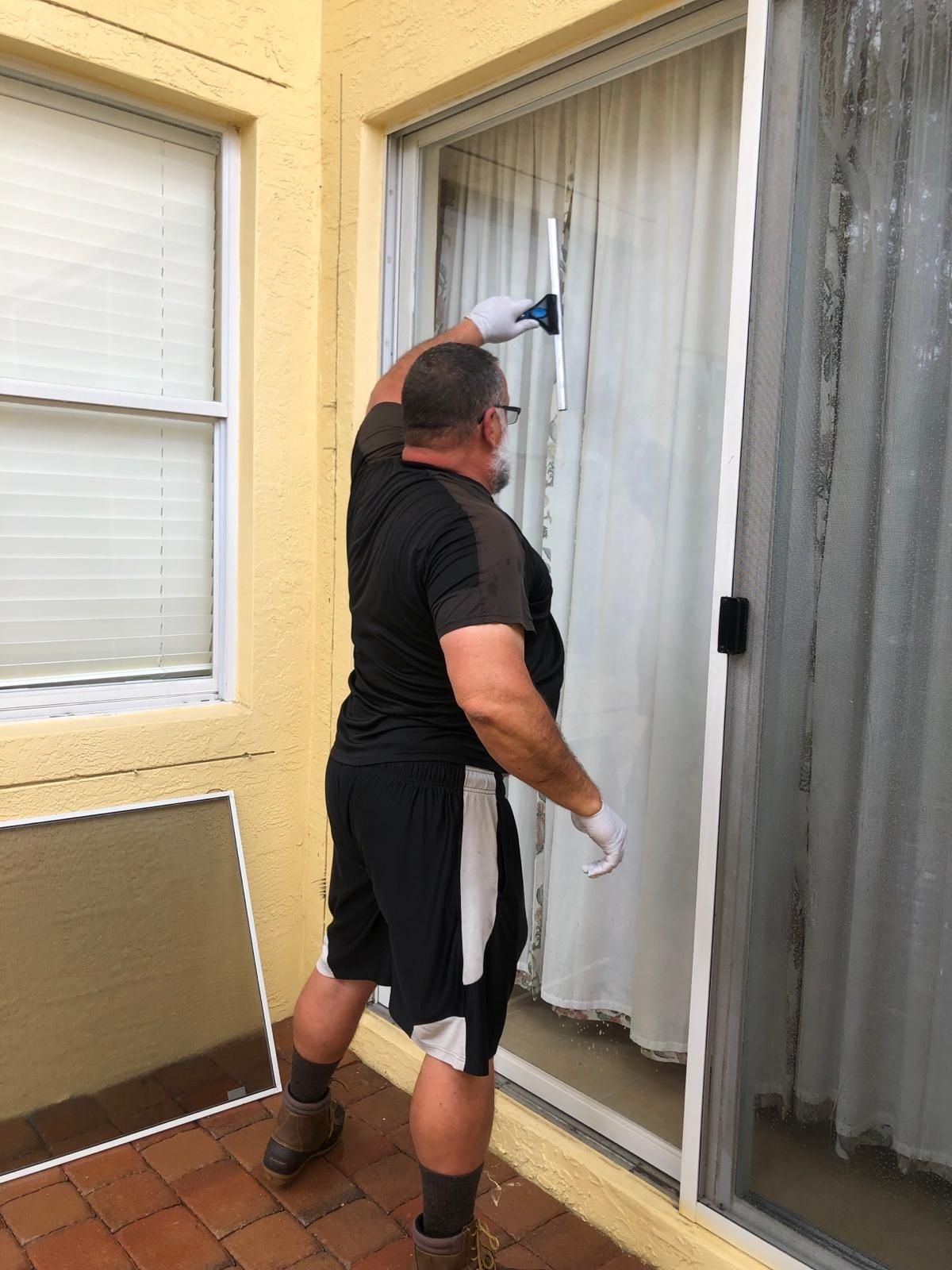 Technician squeegee-cleaning a large sliding glass door, Lake Worth, FL
