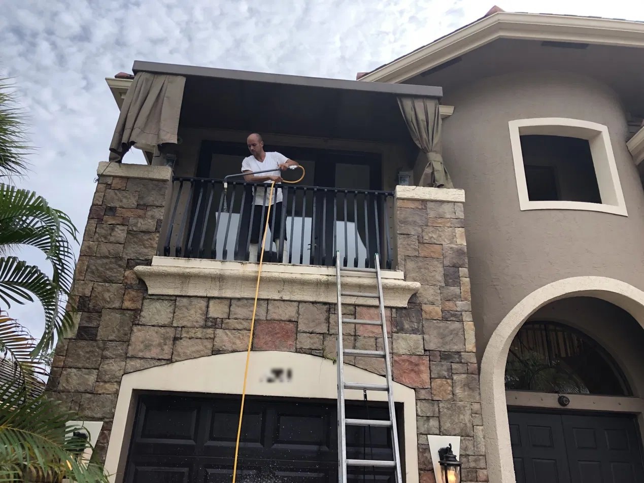 Technician cleaning a second-floor balcony railing during a house wash in Wellington, FL